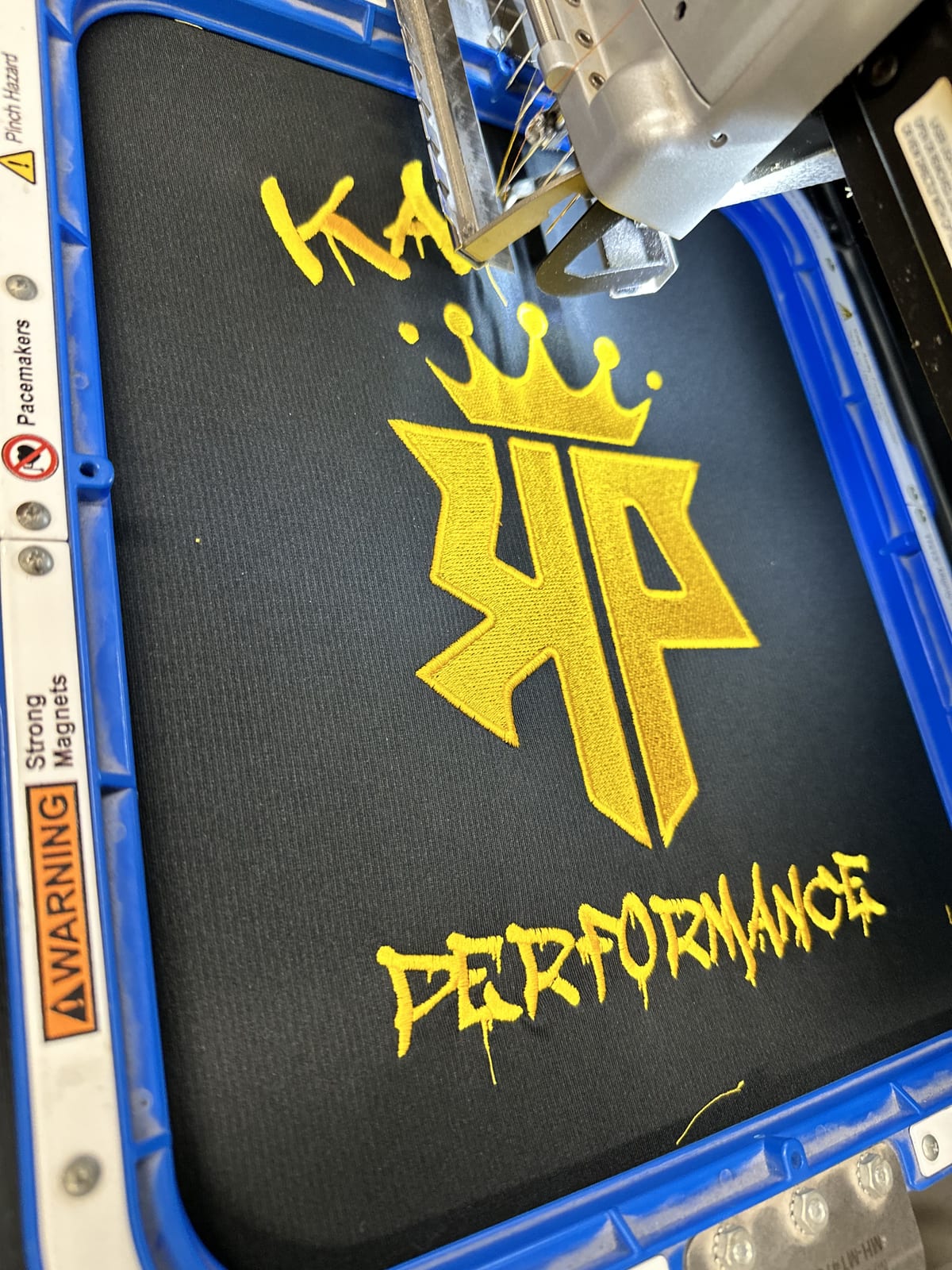 Embroidery head stitching a gold crowned logo on black fabric