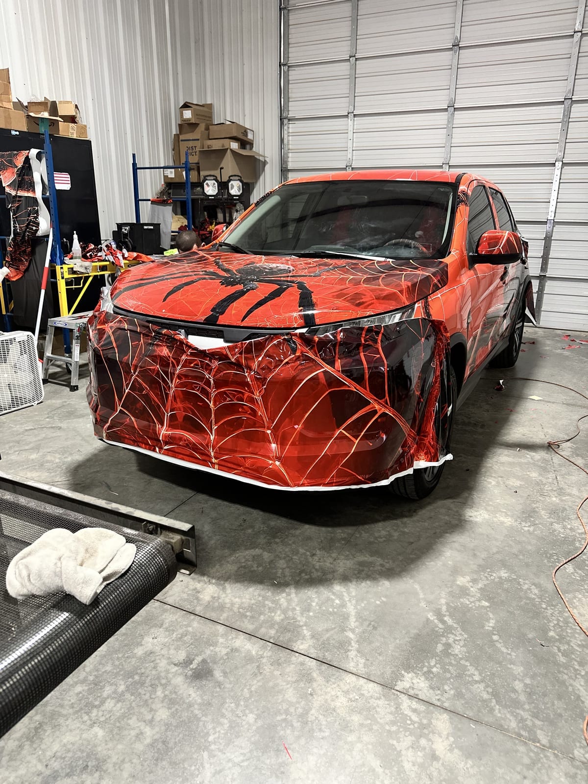 Spider-web art wrap mid-install, printed film untrimmed over the front bumper